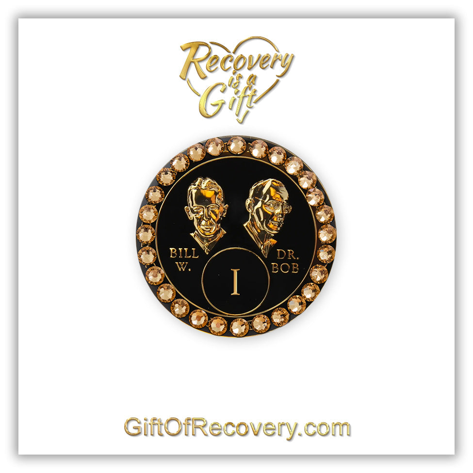 1 year AA Bill & Bob black Onyx recovery medallion with 28 genuine Dorado crystals around the rim, this medallion is to honor our founders and our time, stylized busts of Bill W. and Dr. Bob, with their names, in embossed 14k gold-plated brass, the medallion is sealed with resin for a glossy finish, seen on a white 3x3 card with recovery is a gift going through an open heart at the top and giftofrecovery.com on the bottom, both in the color gold.
