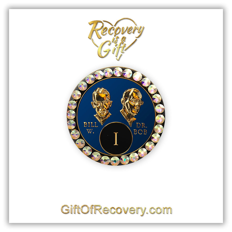 1 year AA Bill & Bob Big Book Blue recovery medallion with 28 genuine Aurora Borealis crystals around the rim, this medallion is to honor our founders and our time, stylized busts of Bill W. and Dr. Bob, with their names, are embossed 14k gold-plated brass, the medallion is sealed with resin for a glossy finish. seen on a white 3x3 card with recovery is a gift going through an open heart at the top and giftofrecovery.com on the bottom, both in the color gold.
