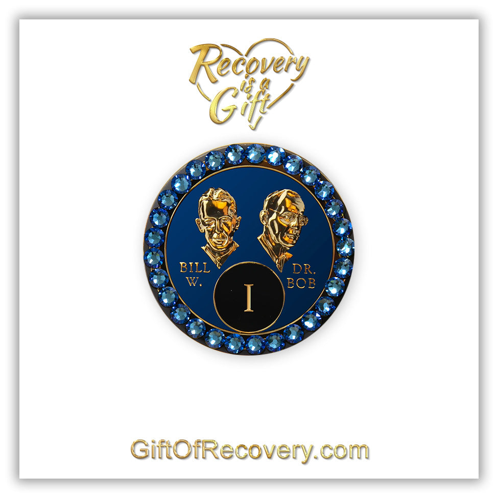 1 year AA Bill & Bob Big Book Blue recovery medallion with 28 genuine Blue crystals around the rim, this medallion is to honor our founders and our time, stylized busts of Bill W. and Dr. Bob, with their names, are embossed 14k gold-plated brass, the medallion is sealed with resin for a glossy finish. seen on a white 3x3 card with recovery is a gift going through an open heart at the top and giftofrecovery.com on the bottom, both in the color gold.