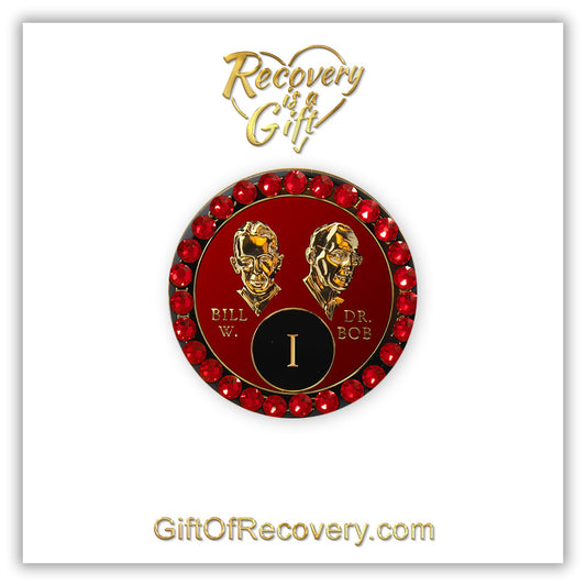 1 year AA Bill & Bob Ruby red recovery medallion with 28 genuine red Siam crystals around the rim, this medallion is to honor our founders and our time,  stylized busts of Bill W. and Dr. Bob, with their names, in embossed 14k gold-plated brass, the medallion is sealed with resin for a glossy finish, seen on a white 3x3 card with recovery is a gift going through an open heart at the top and giftofrecovery.com on the bottom, both in the color gold.