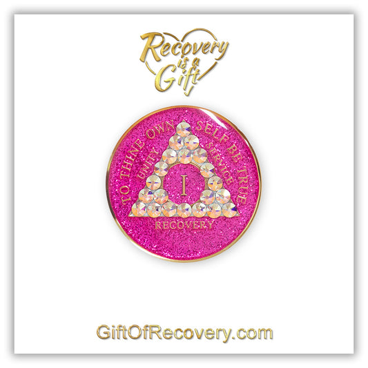1 year AA medallion pink glitter princess adorned with 21 Aurora Borealis genuine crystals to bring out the sober princess in you the crystals are in the shape of the triangle, to thine own self be true and AA moto embossed with 14k gold-plated brass, recovery medallion is sealed with resin for a glossy finish that will last and is scratch proof, featured on a white 3x3 card with recovery is a gift and giftofrecovery.com in the color gold.