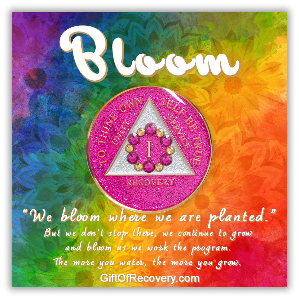 1 year AA medallion princess pink glitter with 6 gold CZ genuine crystals and 6 pink zircon forming a circle around the roman numeral to represent blooming in the program and growing where you are planted, the triangle is pearl white and AA moto is embossed with 14k gold-plated brass, pictured on a bold tie-dye 3x3 card with silhouettes of flowers, the word bloom along with a paragraph describing the meaning behind the recovery medallion, are in the color white.