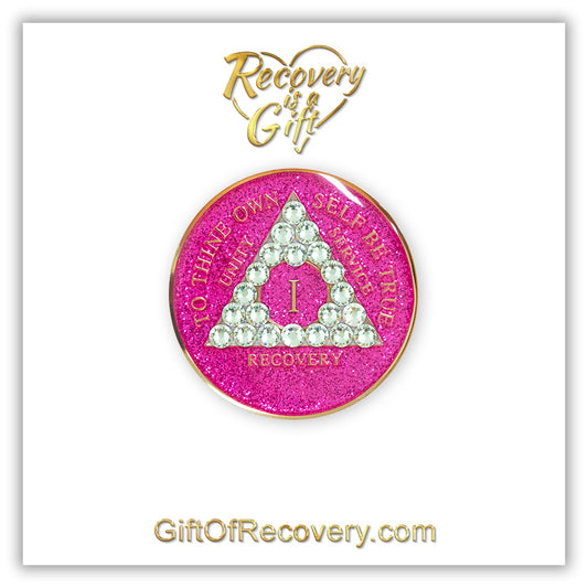 1 year AA recovery medallion in glitter princess pink and adorned with 21 diamond CZ genuine crystals shaped in the triangle to add sparkle to your sober princess journey in recovery, to thine own self be true, unity, service, recovery are embossed with 14k gold-plated brass and sealed with resin for a glossy finish that will last and is scratch proof, featured on a white 3x3 card with recovery is a gift, giftofrecovery.com in the color gold.
