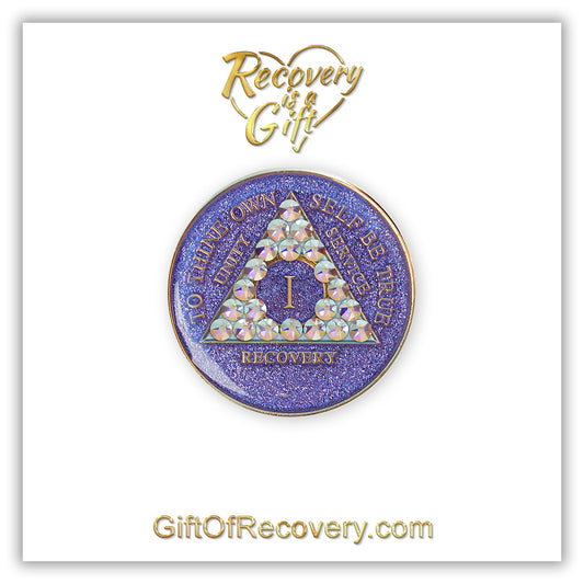 1 year AA medallion Purple glitter with 21 Aurora Borealis genuine crystals in the shape of the triangle, to thine own self be true, unity, service, recovery, the outer rim, and the roman numeral are embossed with 14k gold-plated brass, the recovery medallion is sealed in resin for a shiny finish that lasts, the medallion is featured on a white 3x3 card with recovery is a gift going through a heart at the top center, and giftofrecovery.com on the bottom, both are in the color gold.