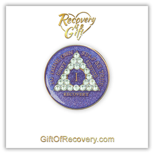 1 year AA medallion purple glitter with 21 genuine diamond CZ crystals in the shape of the triangle, with to thine own self be true, unity, service, recovery, and the roman numeral embossed with 14k gold-plated brass, the recovery medallion is sealed with resin for a shiny finish that will last and is scratch proof, the medallion is featured on a white 3x3 card with Recovery is a Gift going through a heart at the top and GiftOfRecovery.com at the bottom, both writings are in the color gold.