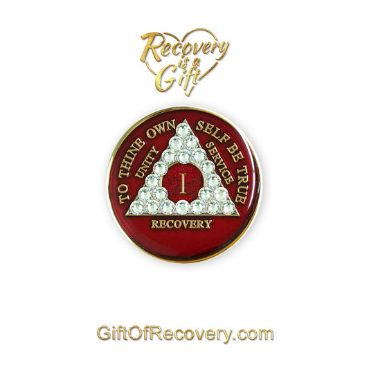 1 year ruby red AA medallion adorned with 21 genuine diamond CZ crystals emphasizing the growth under pressure like true diamonds are formed, to thine own self be true, unity, service, recovery are embossed with 14k gold-plated brass and sealed with resin for a glossy finish that is scratch proof and will last, seen on a white 3x3 card with recovery is a gift going through an open heart at the top and giftofrecovery.com on the bottom, both in the color gold.