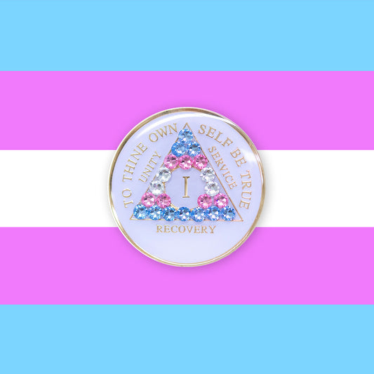 1 Year AA medallion pearl white with 21 genuine crystals that are the colors of the Transgender flag, to represent sobriety and pride for who you are, AA slogan and three legacies are embossed with 14k gold-plated brass and recovery medallion is sealed with resin for a glossy finish, pictured on a 3x3 example of the Transgender flag.
