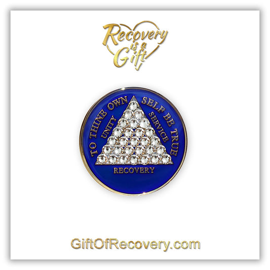 AA medallion Big Book blue with 28 genuine crystals that form the triangle entirely, this is the timeless recovery medallion, shine on with this beauty, we all have one day at a time, the AA slogan and three legacies are embossed with 14k gold-plated brass and sealed with resin for a glossy finish that will last and is scratch proof, pictured on a white 3x3 card with recovery is a gift going through an open heart at the top and giftofrecovery.com at the bottom, both in the color gold.