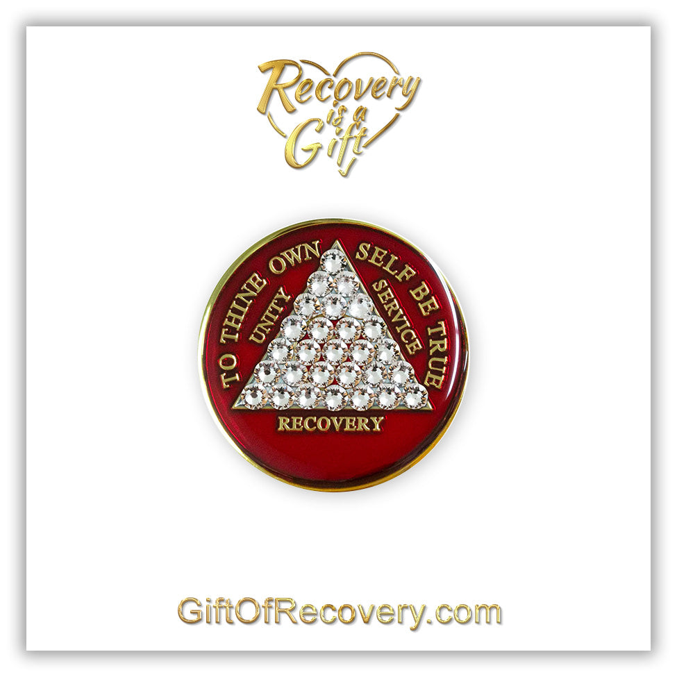 Timeless AA medallion Ruby red with 28 diamond CZ genuine crystals that form the triangle entirely, this is the timeless recovery medallion, shine on with this beauty, we all have one day at a time, the AA slogan and three legacies are embossed with 14k gold-plated brass and sealed with resin for a glossy finish that will last and is scratch proof, pictured on a white 3x3 card with recovery is a gift going through an open heart at the top and giftofrecovery.com at the bottom, both in the color gold.