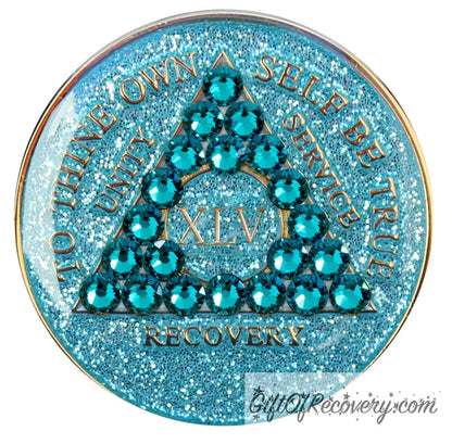 45 year AA medallion in aqua glitter with to thine own self be true, unity, service, recovery, the roman numeral in the center, and the outer rim of the medallion embossed in 14k gold plated brass, the center triangle has 21 genuine blue zircon crystal to give it a sparkle, it is sealed with resin for a shiny finish.