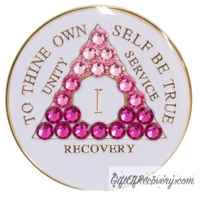 1 year pearl white AA medallion with 21 genuine crystals in the shape of the triangle and ranging from light to dark pink, representing the transformation of your sobriety journey, the AA moto along with the roman numeral and rim of medallion are 14k gold plated brass and sealed with resin for a glossy finish.