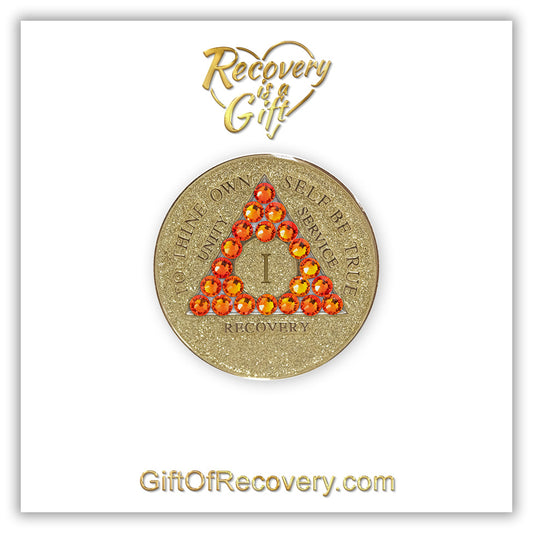 1 year Gold glitter AA medallion with twenty-one fire opal genuine crystals in the shape of a triangle, to thine own self be true, unity, service, recovery embossed in 14k gold-plated brass along with the rim of the medallion, sealed in a high-quality, chip and scratch-resistant resin dome giving it a beautiful glossy look that will last, it is featured on a white 3x3 card with recovery is a gift and giftofrecovery.com.