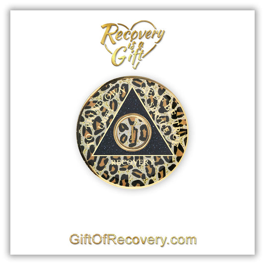 1 year AA medallion leopard print with gold flaked spots, to thine own self be true, unity, service, recovery, and roman numeral are gold foil so you can let your recovery shine, not your time, the circle triangle is embossed with 14k gold-plated brass, the recovery medallion is sealed with resin for a shiny finish, the medallion is featured on a white 3x3 card with recovery is a gift going through a heart at the top and GiftOfRecovery.com on the bottom, both in the color gold. 