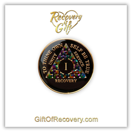 1 year black onyx AA recovery medallion, with 21 genuine peacock crystals, symbolizing the beauty and diversity of recovery journeys, the AA medallion has; to thine own self be true, unity, service, recovery, roman numeral, and the rim, embossed with 14k gold and sealed with resin for a glossy finish. The Recovery medallion is placed on a white 3x3 card with recovery is a gift in the middle of a heart, in the color gold. 