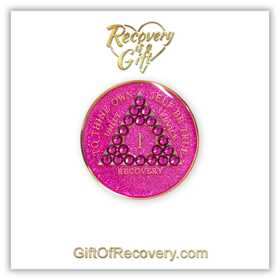 1 year Princess Pink Glitter AA medallion with 21  genuine fuchsia crystals in the shape of a triangle in the center of the recovery medallion, and to thine own self be true, unity, service, recovery, the roman numeral in the middle, and the outer rim, embossed in 14k plated brass, the aa medallion is sealed in resin for a shiny finish, the recovery medallion is on a 3x3 white card with recovery is a gift going through a heart at the top and giftofrecovery.com at the bottom, all in color gold. 