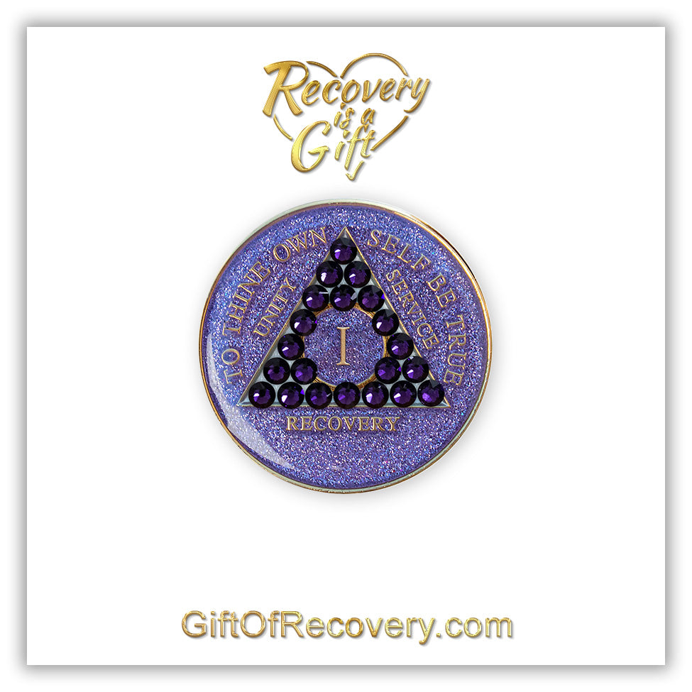 1 year glitter purple AA medallion with 21 purple velvet genuine crystals, and to thine own self be true, unity, service, recovery, the roman numeral in the center of the circle triangle, along with the rim of the recovery medallion, are embossed in 14 gold plated brass, the medallion is on a white 3x3 card with the words recovery is a gift inside a heart in the color gold.