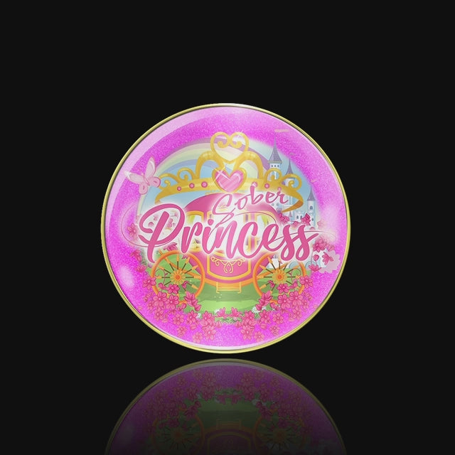 Sober princess AA medallion with a pink and gold carriage, set on grass with pink flowers, a castle in the back ground with a pink rainbow above it all, the crown has one big pink heart in the center and 3 pink dots on either side, calling all sober princess, the medallion is on a black background and slowly spinning to depict the recovery medallion accurately. 