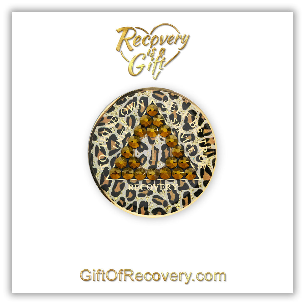 1 year AA medallion in leopard print with gold flake glitter spots and 21 genuine dorado crystals shaped in a triangle around the year, the outer rim is 14k gold and the unity, service, recovery, To thine own self be true and the year is 14k gold foil, the recovery medallion is set on a white 3x3 card and has recovery is a gift going through a heart shape and giftofrecovery.com in color gold. 
